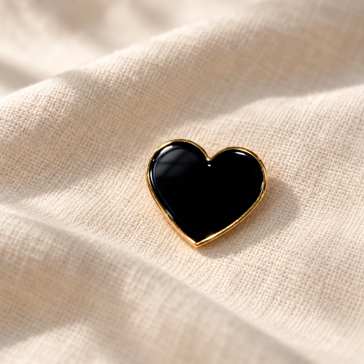 Close-up of the black enamel and gold Mourning Heart pin resting on natural linen